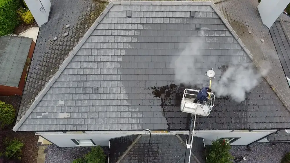 Soft washing a tiled roof from a cherry picker, with the cleaned part of the roof next to the part still to be done